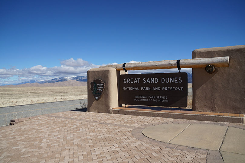 Great Sand Dunes National Park and Preserve sign with the dunes in the background to the left.
